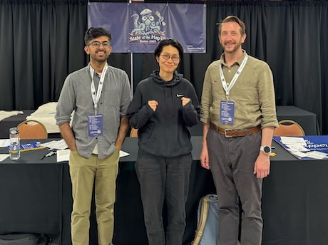 Three people pose in front of a State of the Map US banner